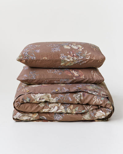 A stack of three bedding items, including two pillows and a folded duvet cover, in a brown floral pattern on a light gray background.