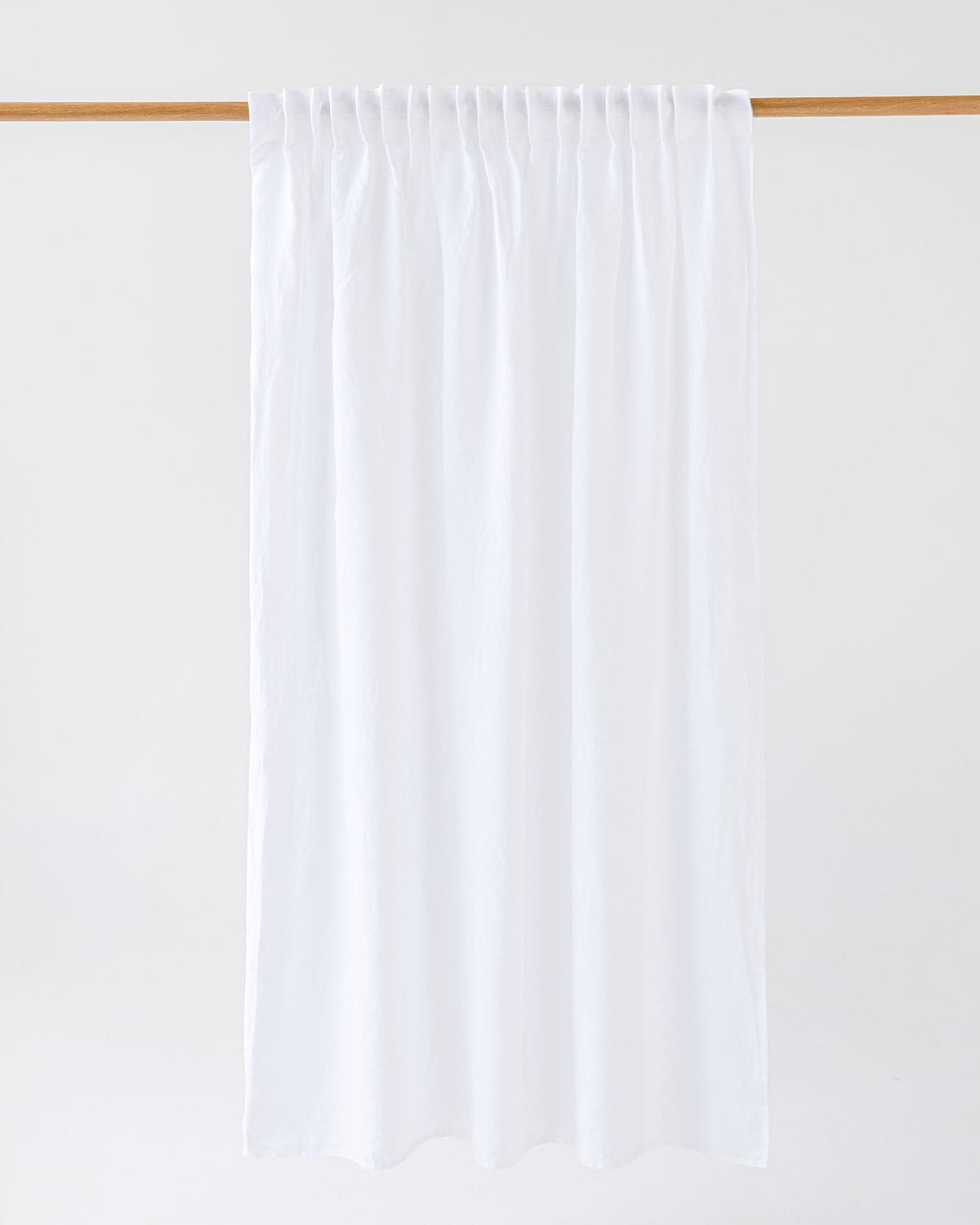 A white pleated curtain panel hanging from a light wood rod against a clean white background.